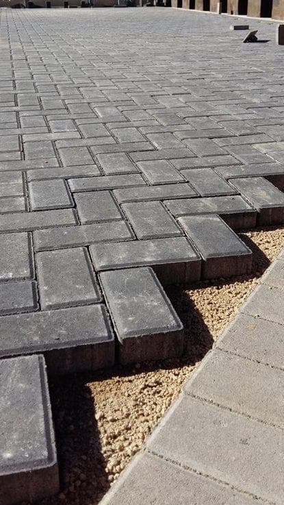 Grey herringbone paving bricks mid-installation